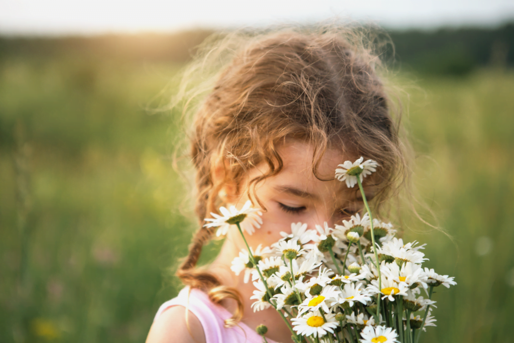 Ein junges Mädchen riecht an einem Blumenstrauß auf einer Wiese. Verdacht auf Pollenallergie