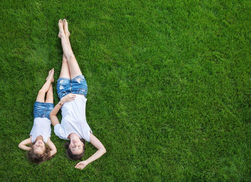 Grasmilben; eine Mutter, die sich mit ihrer Tochter auf einem frischen, grünen Rasen entspannt