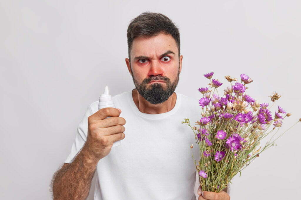 Mann mit Heuschnupfen, Pollenallergie hält Inhalator und Blumen, Gräser in der Hand